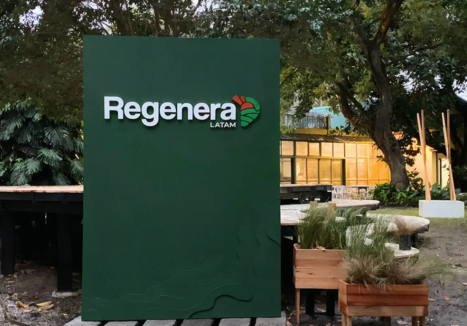 El panel verde de Regenera LATAM entre canteros y bancos del predio