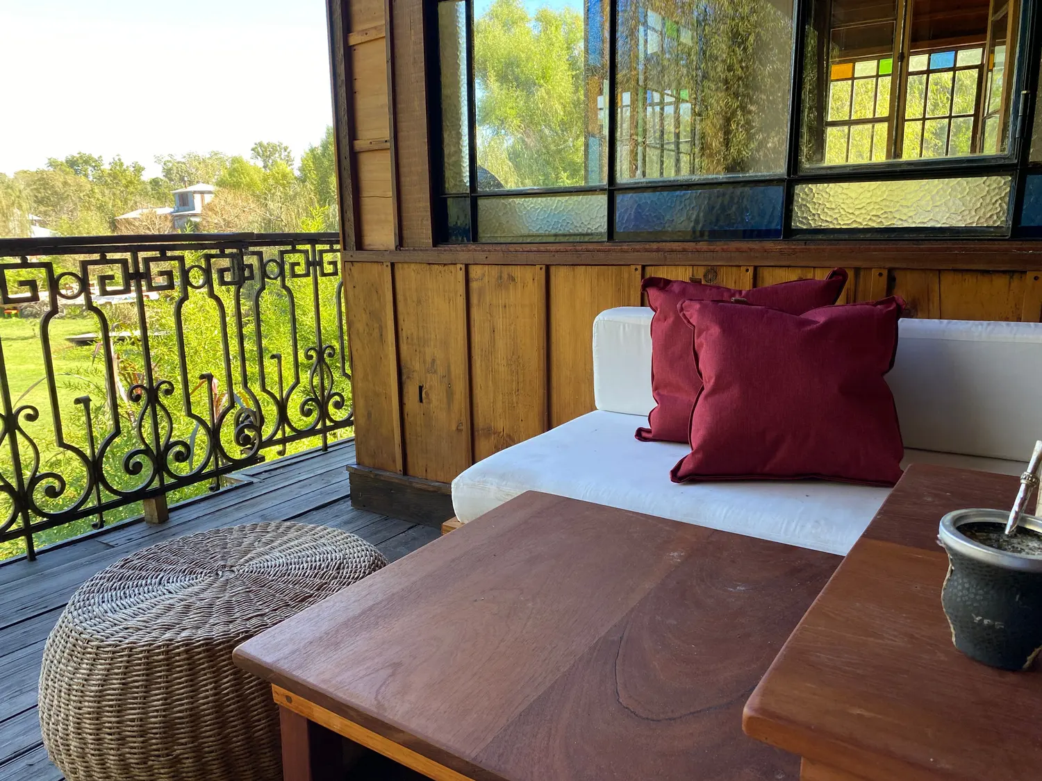 Sillón blanco con almohadones bordó junto a la baranda de hierro, con vista al jardín