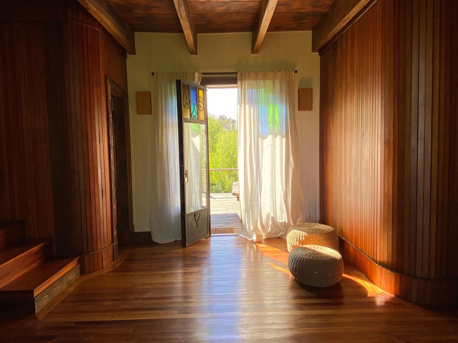 Pasillo de madera con vigas a la vista que lleva a la puerta abierta al deck