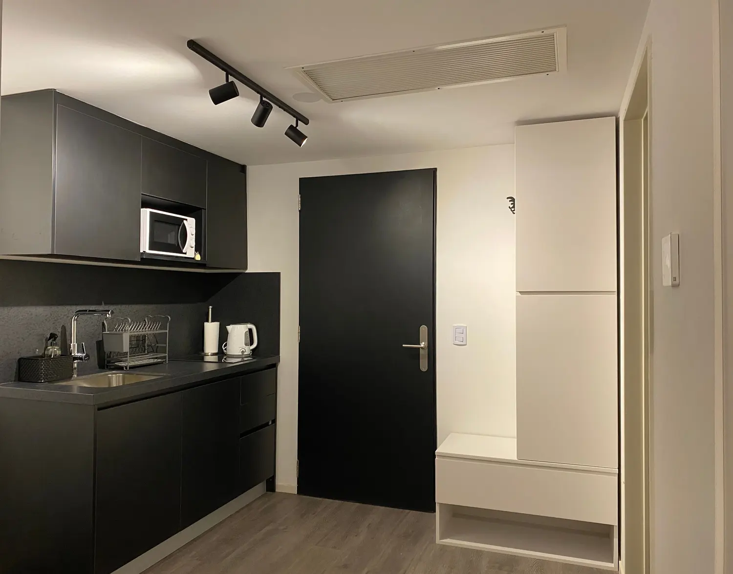 Kitchenette negra con microondas y luces de riel, junto a la puerta de entrada